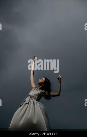 Vue en angle bas de la femme dansant avec les bras levés sur la terrasse contre les nuages de tempête Banque D'Images