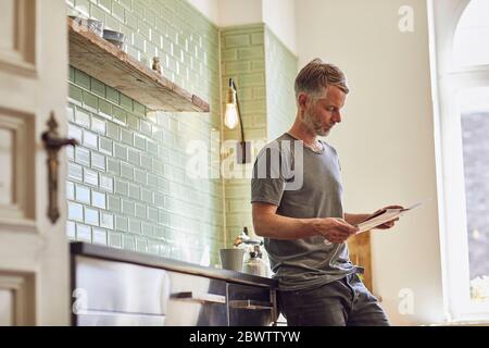 Homme mature lisant le journal dans la cuisine à la maison Banque D'Images