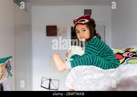 Portrait de petite fille avec masque de renard assis sur un lit superposé pieds nus à la maison Banque D'Images