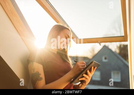 Jeune femme utilisant une tablette graphique à la fenêtre en contre-jour Banque D'Images