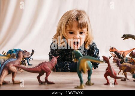 Portrait d'une petite fille qui est couché sur le sol et qui joue avec des dinosaures Banque D'Images