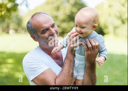 Homme senior souriant tenant une petite fille dans un parc Banque D'Images