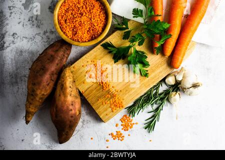 Studio de coupe, bol de lentilles rouges, patates douces, carottes, romarin, persil et ail Banque D'Images