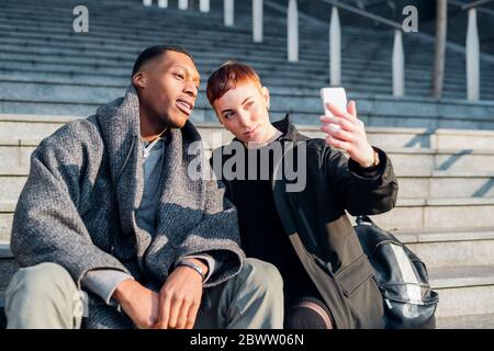 Jeune couple assis sur les escaliers dans la ville en prenant un selfie Banque D'Images