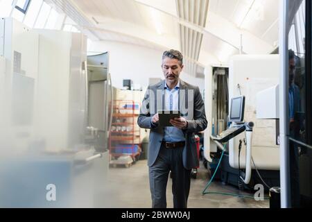 Homme d'affaires mature qui se promère dans l'usine, en utilisant une tablette numérique Banque D'Images