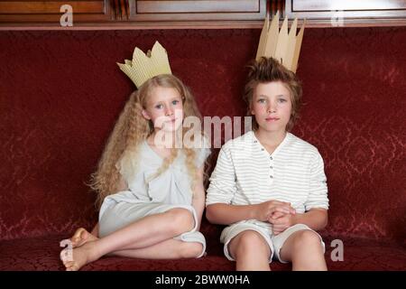 Garçon et fille assis sur un canapé portant des couronnes en carton Banque D'Images