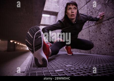 Une athlète féminine s'échauffe avant de courir dans un passage souterrain pour piétons Banque D'Images