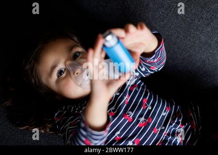 Portrait grand angle de la jeune fille asthmatique utilisant un inhalateur tout en étant allongé sur un canapé dans le salon à la maison Banque D'Images