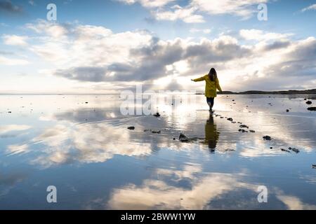 Femme marchant au milieu de la mer avec réflexion à Hvalnes nature Reserve Beach, Islande Banque D'Images