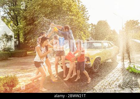 Amis lavant la voiture jaune vintage en été s'amuser Banque D'Images