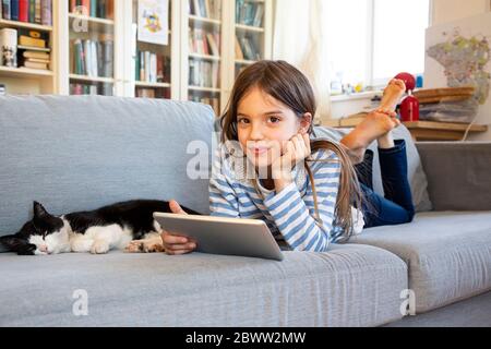 Portrait d'une fille souriante couché sur un canapé avec un chat et une tablette numérique Banque D'Images