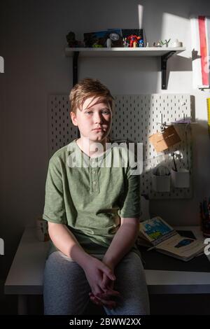 Portrait d'un garçon sérieux assis sur un bureau à la maison Banque D'Images