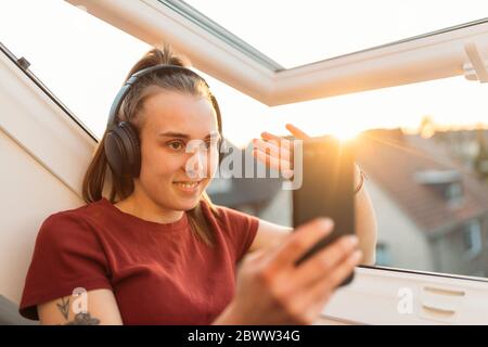 Jeune femme ayant un chat vidéo à la fenêtre en contre-jour Banque D'Images
