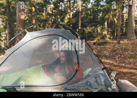 Jeune femme en tente isn la forêt, boire du thé Banque D'Images