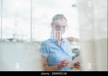 Portrait d'une femme souriante avec tablette numérique derrière un panneau de fenêtre à la marina, Majorque, Espagne Banque D'Images