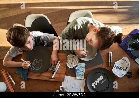 Frère et sœur à la maison, peignant de la vaisselle avec de la peinture en porcelaine Banque D'Images