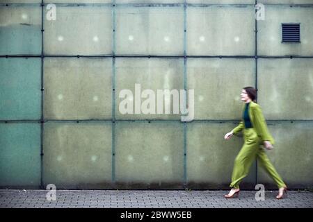 Femme d'affaires portant un costume vert passant devant un mur Banque D'Images