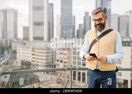 Homme utilisant un smartphone devant des gratte-ciels, Francfort, Allemagne Banque D'Images