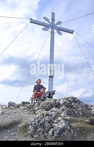 Vue à angle bas de la femme assise sur le banc par la croix au sommet de la montagne Kramerspitz contre le ciel Banque D'Images