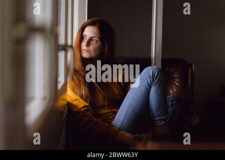 Portrait d'une femme à tête rouge assis à une fenêtre ouverte regardant la maison à distance Banque D'Images