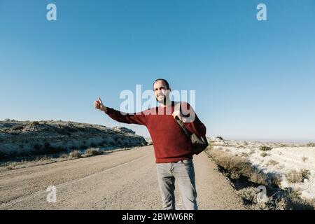 Homme en faisant des gestes tout en s'accrotant sur la route dans le désert contre un ciel bleu clair Banque D'Images