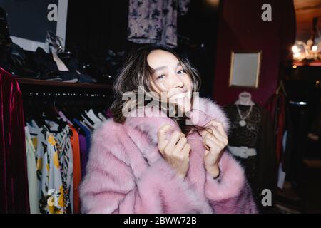 Portrait d'une femme souriante portant une veste en fourrure rose au magasin thrift Banque D'Images