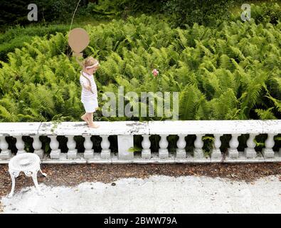 Petite fille marchant sur une balustrade tenant un ballon en carton Banque D'Images