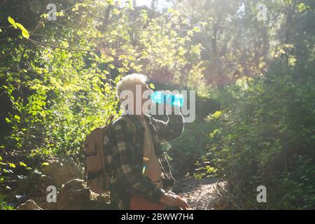 Homme âgé avec sac à dos de l'eau potable de bouteille dans la forêt Banque D'Images