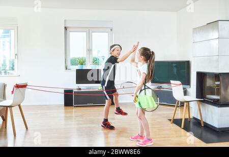 Joyeux frères et sœurs qui donnent cinq personnes en jouant au tennis à la maison en situation de pandémie Banque D'Images