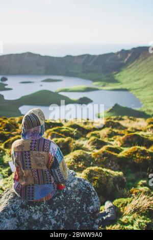 Portugal, Açores, jeune femme assise sur un rocher en admirant le paysage volcanique de Caldeirao