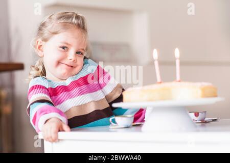 Fille souriante assise à table avec gâteau d'anniversaire Banque D'Images