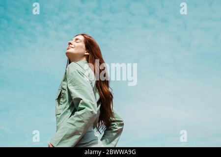 Portrait de jeune femme à tête rouge avec les yeux fermés contre le ciel Banque D'Images