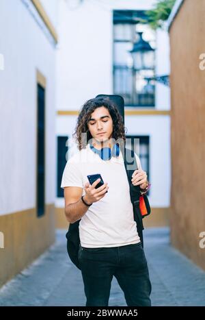 Jeune homme utilisant un téléphone portable tout en se tenant dans une rue étroite à Santa Cruz, Séville, Espagne Banque D'Images