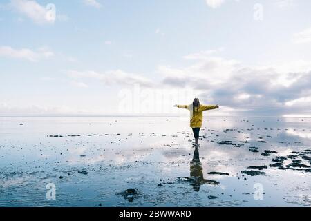 Femme aux bras étirés se reflétant en mer à la plage de la réserve naturelle de Hvalnes, en Islande Banque D'Images