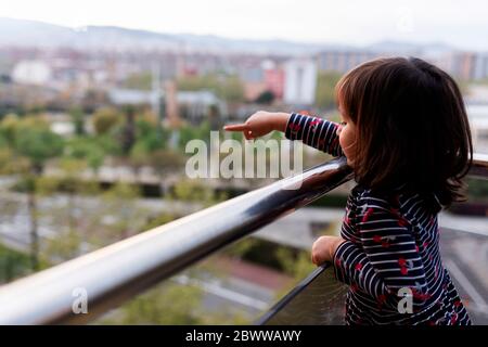 Petite fille debout sur le balcon pointant sur quelque chose Banque D'Images