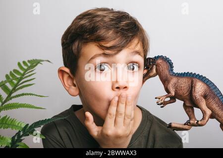 Portrait d'un petit garçon avec un dinosaure jouet tirant sur le visage drôle Banque D'Images