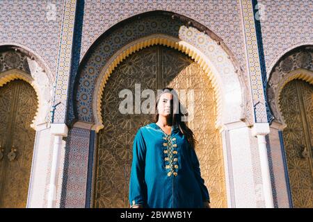 Jeune femme debout devant des archades traditionnelles portant une robe marocaine, Maroc Banque D'Images