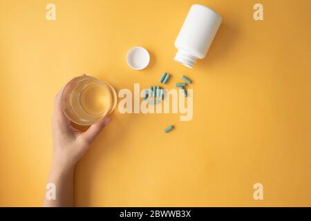 Studio de prise de capsules de supplément nutritionnel et main de femme ramassant un verre d'eau Banque D'Images