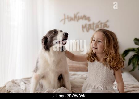 Portrait d'une petite fille assise sur le lit avec son chien Banque D'Images