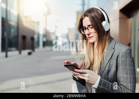 Jeune femme d'affaires avec casque utilisant un smartphone dans la ville Banque D'Images