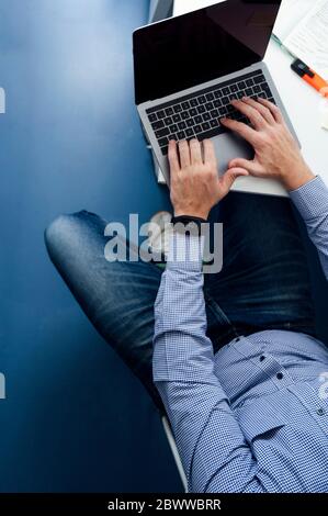 Partie basse de l'homme assis au bureau et tapant sur un ordinateur portable Banque D'Images
