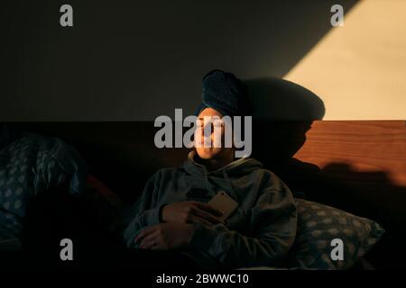 Jeune femme avec la tête enveloppée dans une serviette couchée dans le lit à la maison Banque D'Images