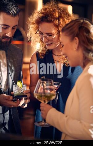 Amis avec cocktails et smartphone en train de rencontrer dans un bar Banque D'Images