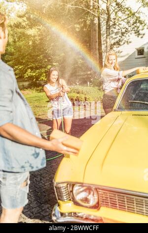 Amis lavant la voiture jaune vintage en été s'amuser Banque D'Images