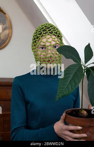 Portrait d'une adolescente portant une coiffure crochetée verte tenant une plante d'avocat en pot Banque D'Images