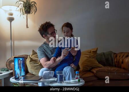 Homme tenant un thermomètre assis avec une fille malade pendant un appel vidéo à la maison Banque D'Images