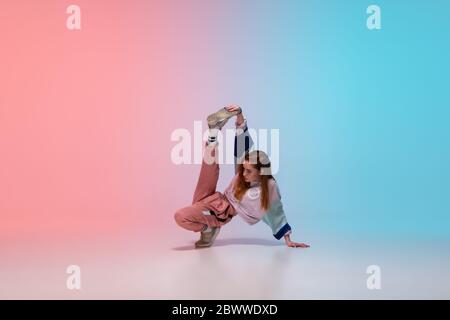 Belle jeune fille dansant hip-hop dans des vêtements élégants sur fond de dégradé coloré à la salle de danse à la lumière du néon. Culture, mouvement, style et mode de jeunesse, action. Portrait lumineux tendance. Banque D'Images