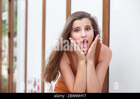 Une jeune femme sur fond de magasin de vêtements urbains est choquée par ce qu'elle voit, elle tient ses mains près de son visage sur les joues à la bouche ouverte. Fille stupéfaite Banque D'Images