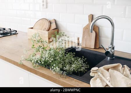 Gros plan de l'intérieur de la cuisine. Mur de briques blanches, carreaux de métro, comptoirs en bois avec planches à découper. Plantes de persil de vache dans évier noir. Moderne Banque D'Images