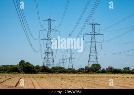 Regarder en bas d'une double rangée de pylônes d'électricité haute tension traversant des champs contre un ciel bleu Banque D'Images